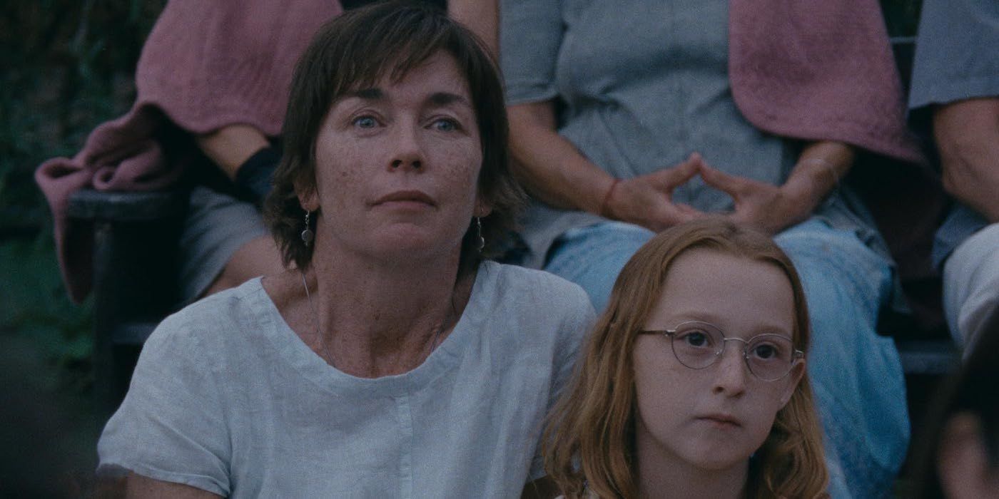 Julianne Nicholson as Janet and Zoe Ziegler as Lacy sitting together while watching a play in a still from Janet Planet. 