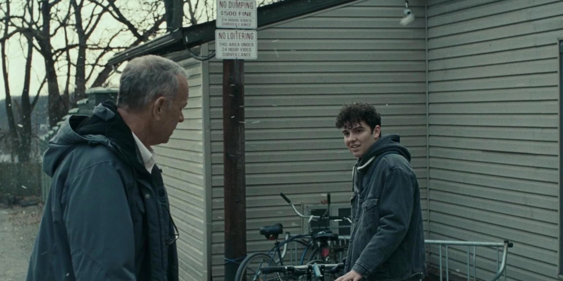 Otto (Tom Hanks) speaking with Malcolm (Matt Bayda) near a bike rack outside in A Man Called Otto