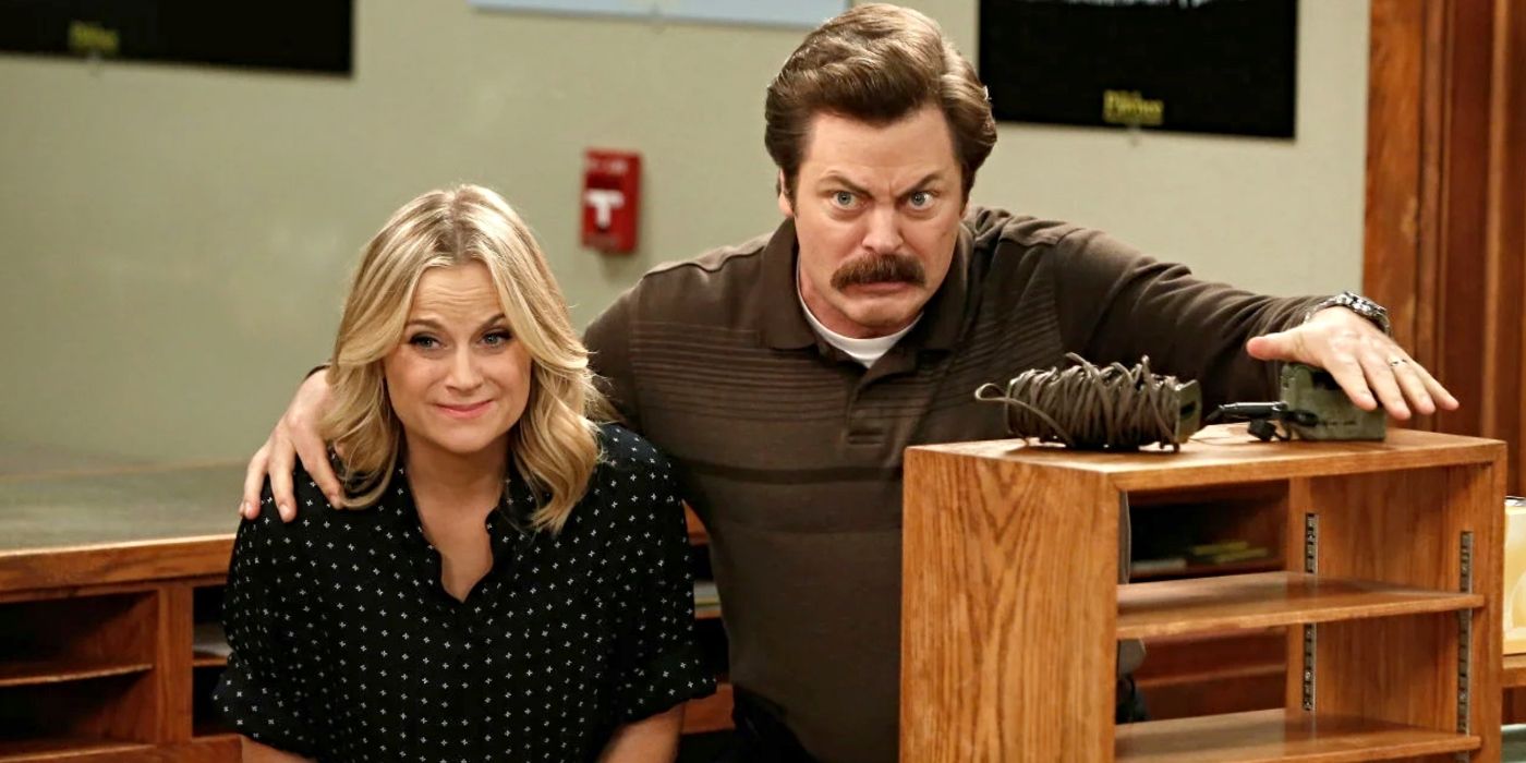 Amy Poehler and Nick Offerman as Leslie Knope and Ron Swanson, standing behind a bookshelf and looking concerned in Parks and Recreation