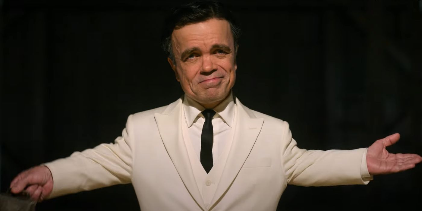 Peter Dinklage wearing a white suit and spreading his arms out in Unfrosted.