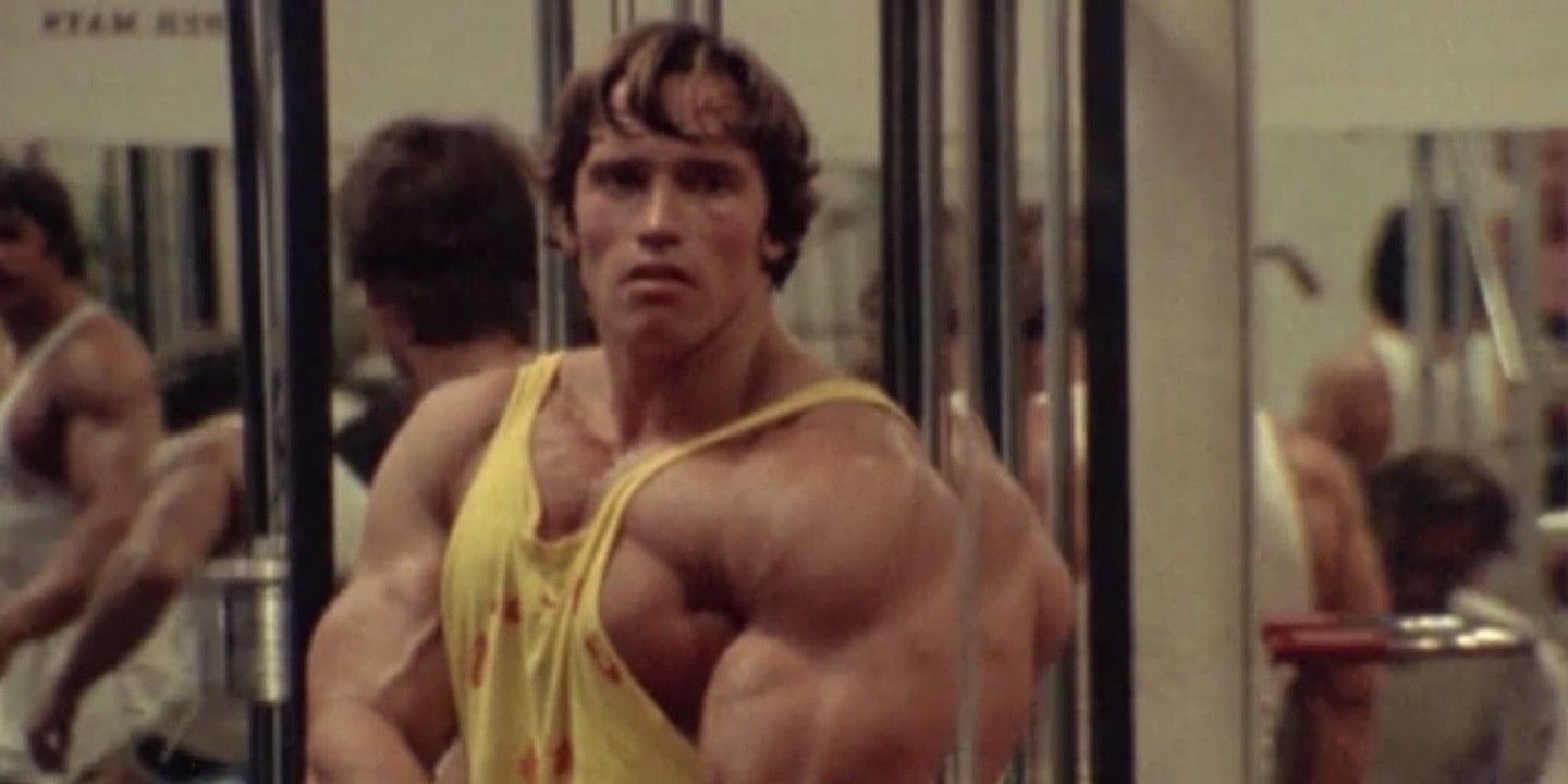 Arnold Schwarzenegger mirant-se al mirall mentre flexiona els músculs del braç a Pumping Iron