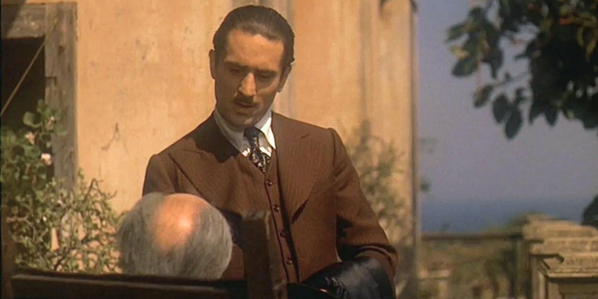 Robert De Niro standing in front of an elderly man in The Godfather: Part II (1974)