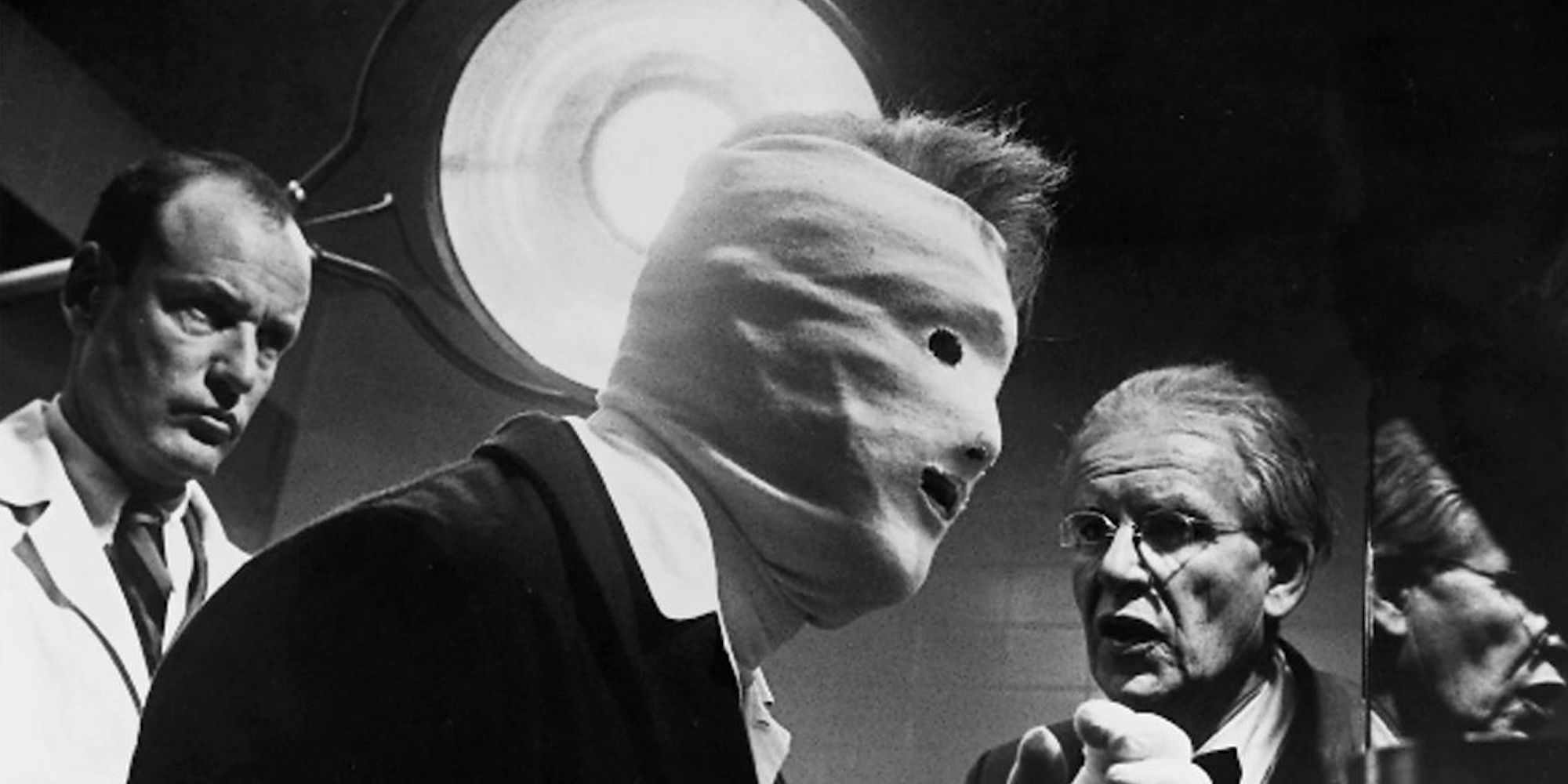 Two men looking at a man with a bandaged face in Seconds