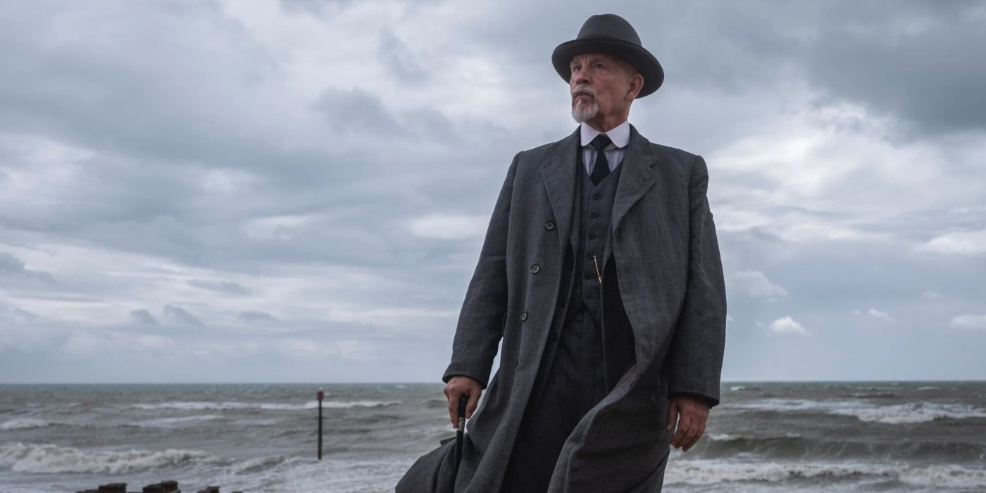 John Malkovich as Hercule Poirot, standing on a beach in The ABC Murders