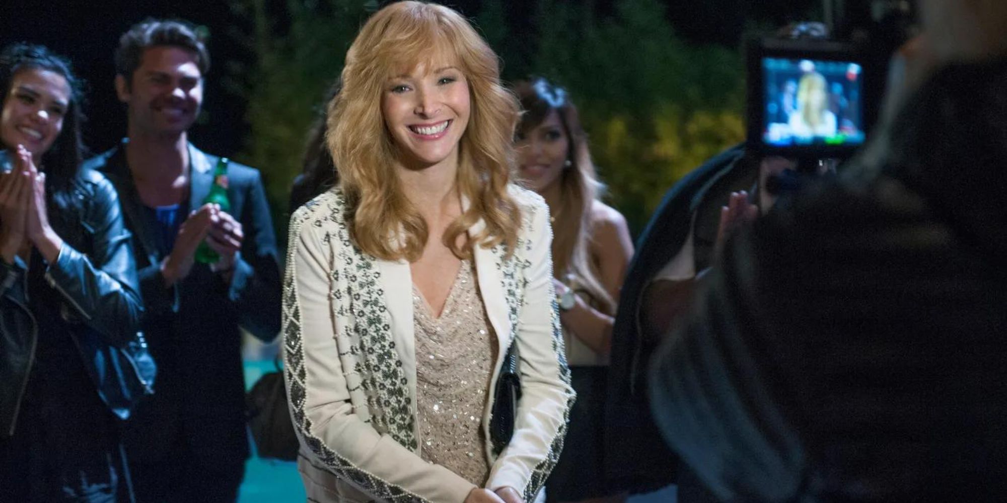 Valerie Cherish (Lisa Kudrow) from The Comeback standing, smiling at the cameras