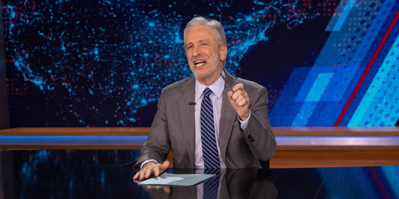 Jon Stewart sitting at The Daily Show desk 