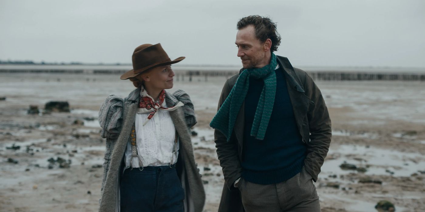 Cora Seaborne (Claire Danes) and Will Ransome (Tom Hiddleston) walking side by side on a marsh beach and looking at one another with mutual smiles in The Essex Serpent