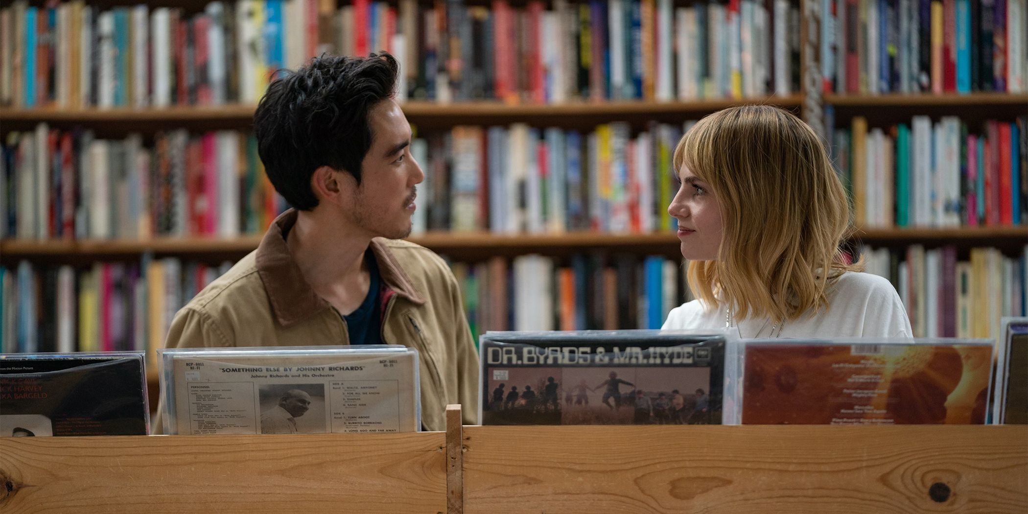 Justin Min and Lucy Boynton looking at each other and smiling in a record shop in The Greatest Hits
