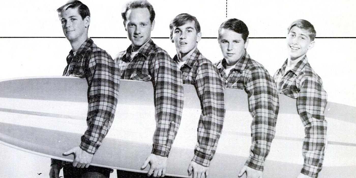 The Beach Boys wearing plaid shirts and holding a surfboard