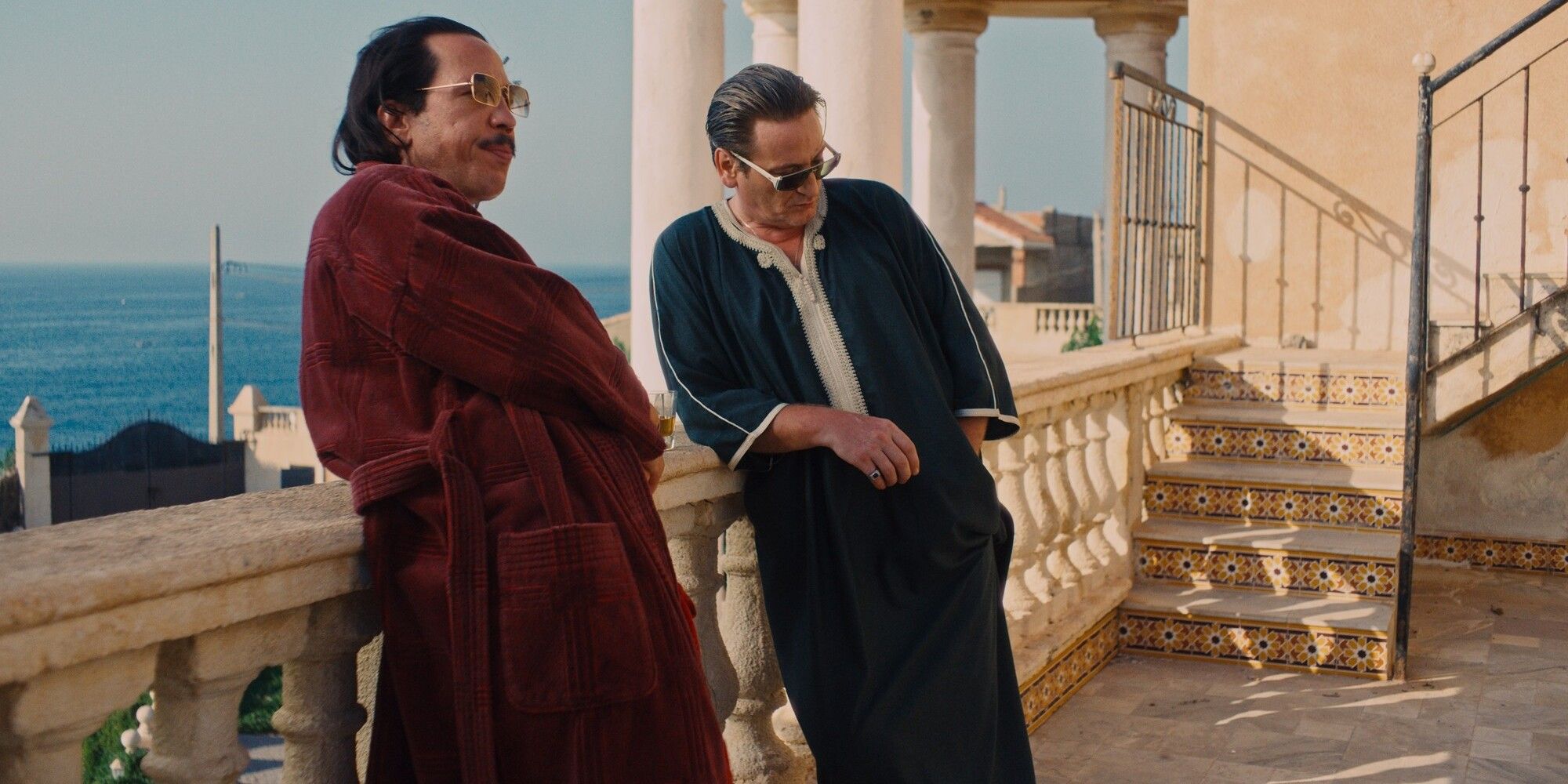 A still from The King of Algiers featuring two men leaning on a balcony with a gorgeous ocean view
