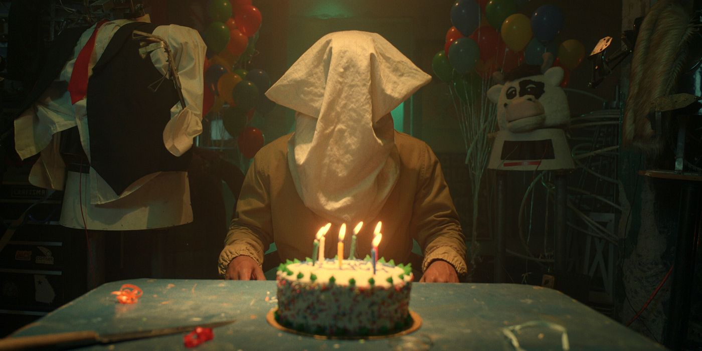 Un hombre con una funda de almohada en la cabeza se sienta frente a un pastel de cumpleaños en Them: The Scare Season 2