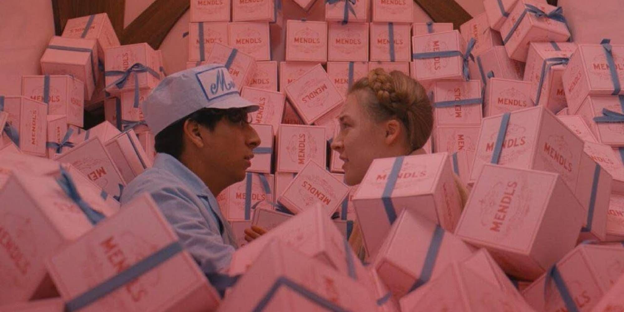 Tony Revolori and Saoirse Ronan in The Grand Budapest Hotel surrounded by pink boxes.