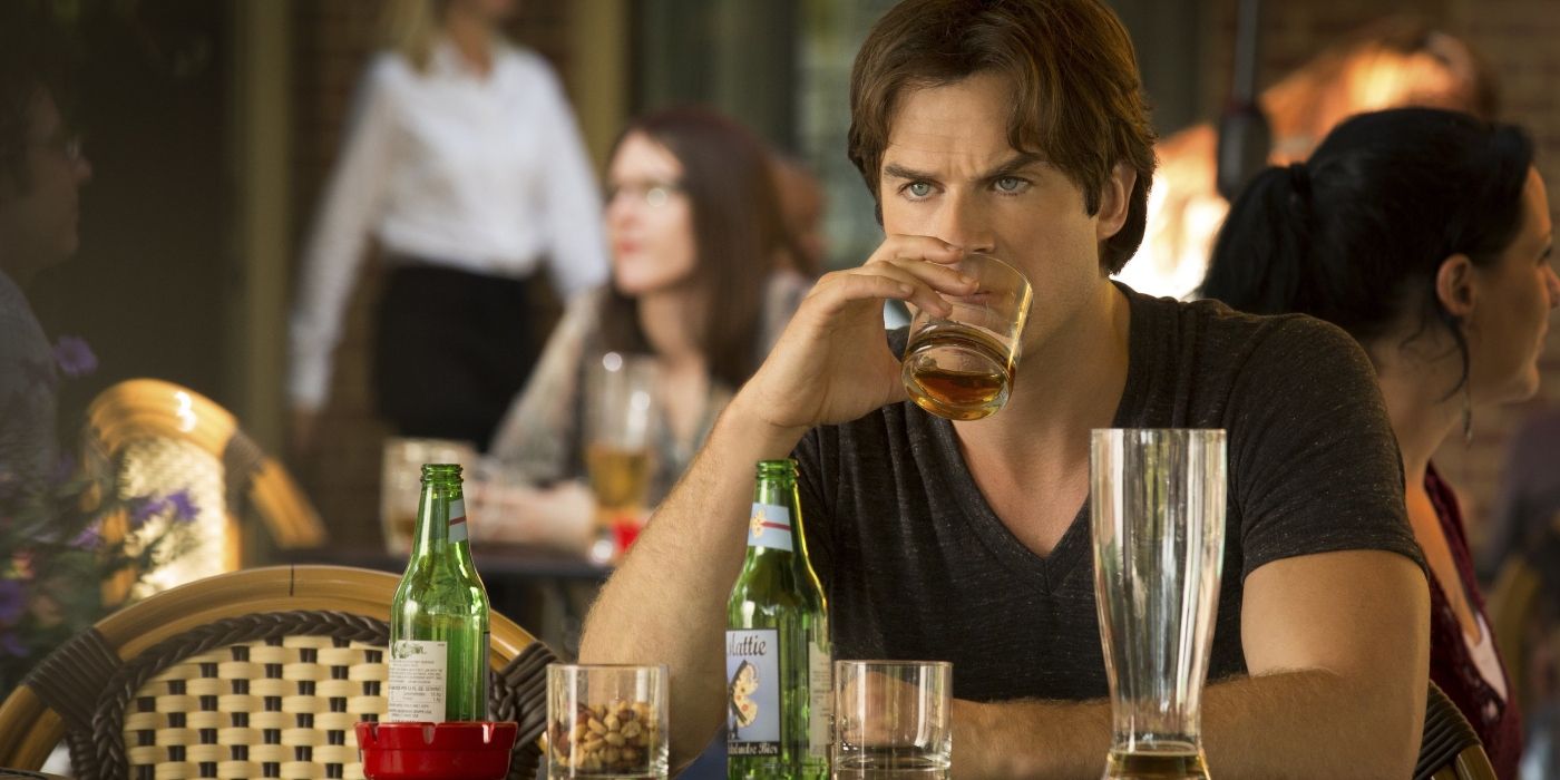 Ian Somerhalder as Damon Salvatore, looking sad and drinking, surrounded by alcohol bottle in the Season 7 premiere of The Vampire Diaries
