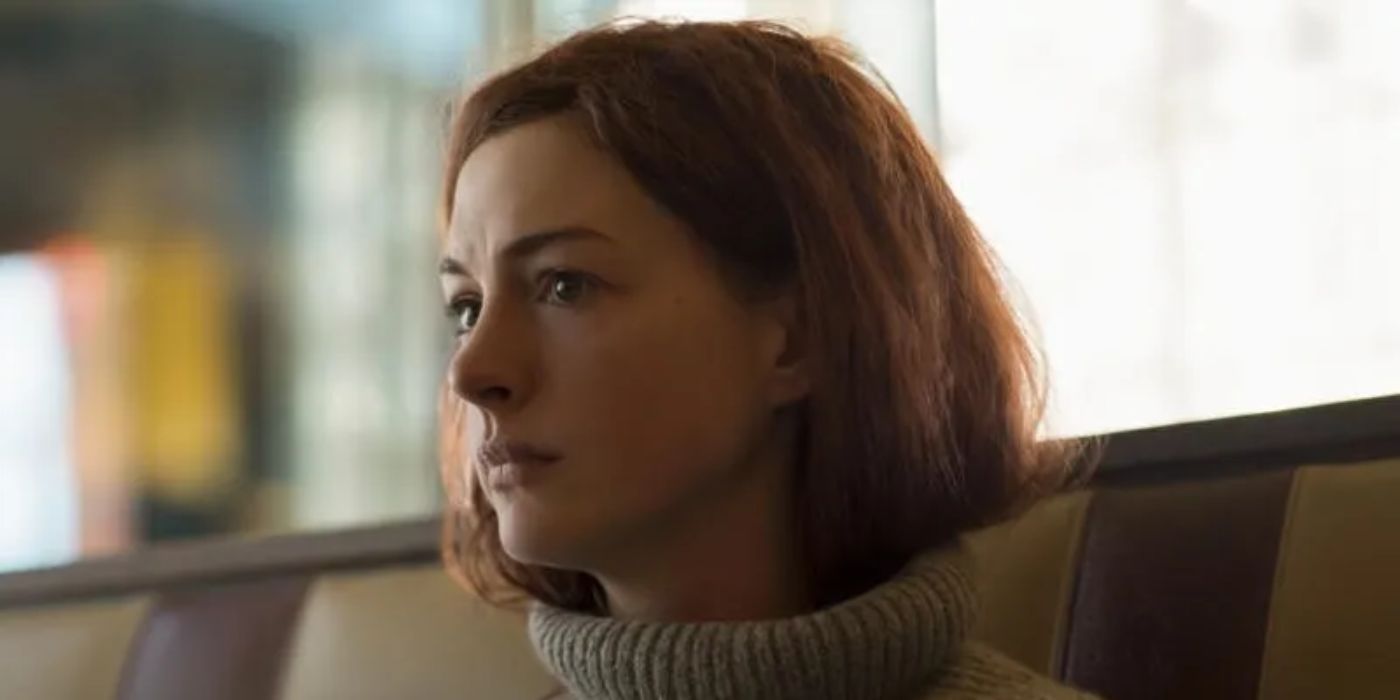 A close-up shot of Anne Hathaway with her hair tucked into her grey, turtleneck sweater.
