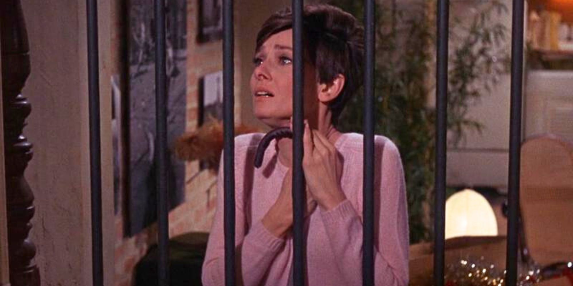 Audrey Hepburn looking scared, standing behind an iron gate in Wait Until Dark (1967).