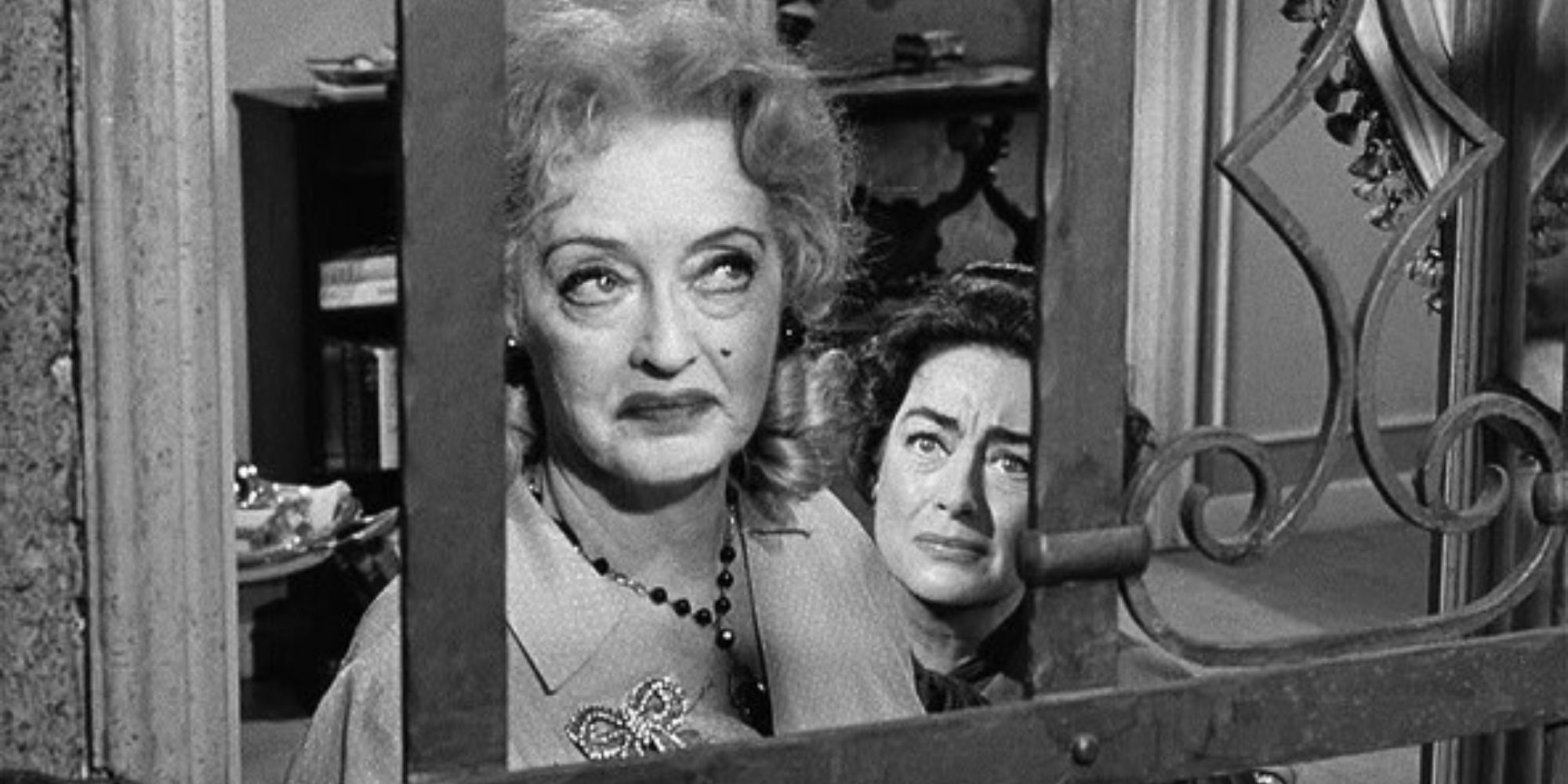 Bette Davis looking out a barred window with Joan Crawford sitting behind her in What Ever Happened to Baby Jane? (1962)