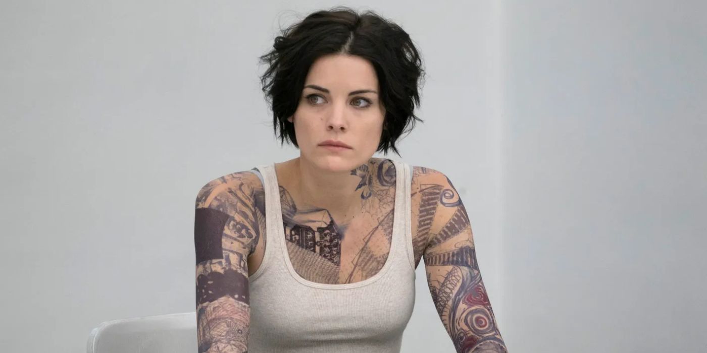 En Blindspot (2015-2020), una mujer muy tatuada, Jane Doe (Jamie Alexander), se sienta en una camiseta en una sala de interrogatorios del FBI, esperando ser interrogada.