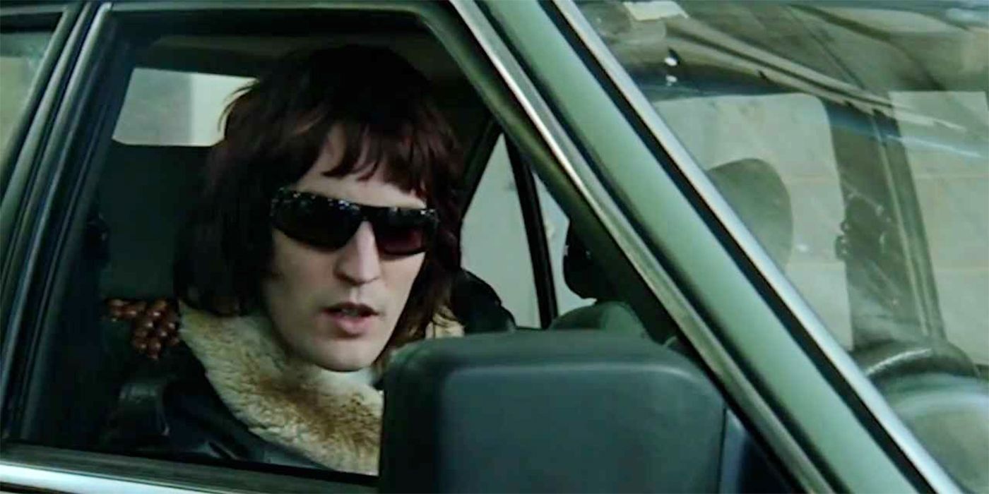 Noel Fielding sentado en un automóvil con gafas de sol y mirando a la cámara en Blue Song de Mint Royale