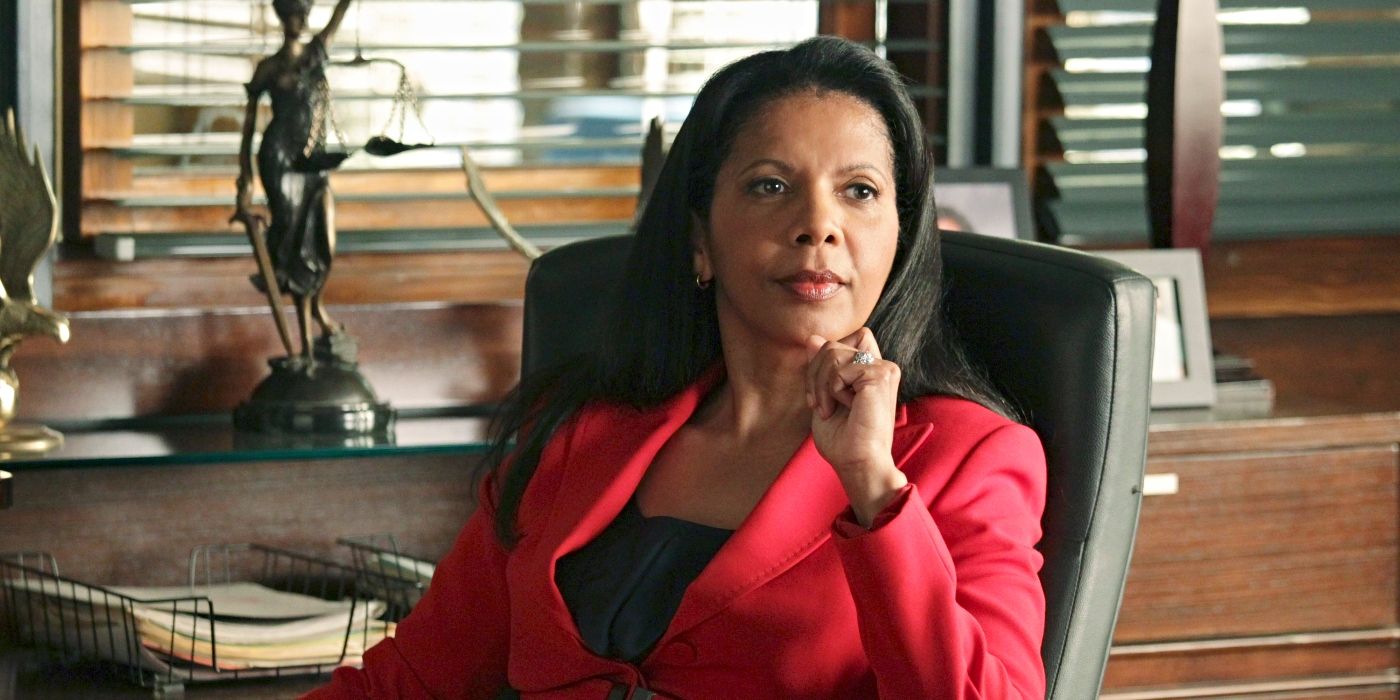 Penny Johnson Jerald as Captain Victoria Gates, sitting at a desk wearing a red jacket on Castle
