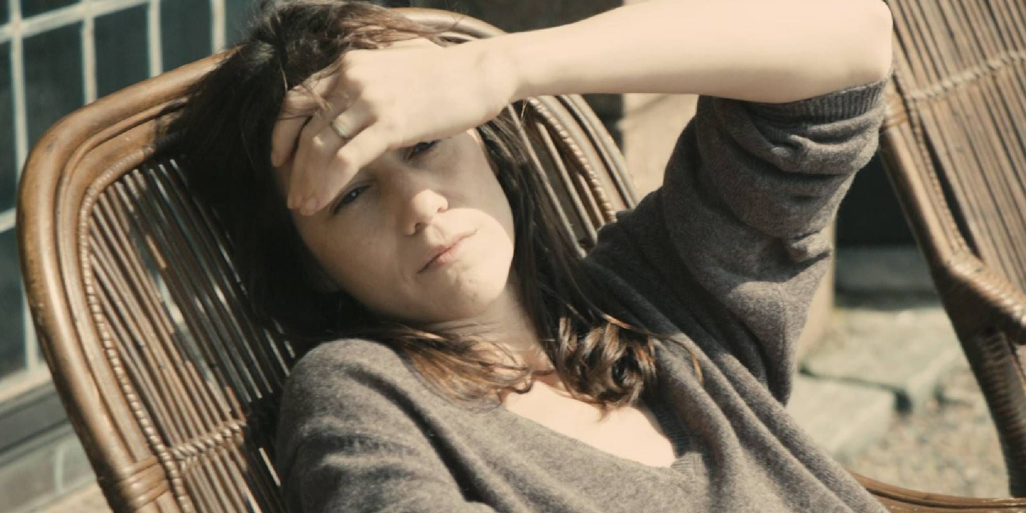 Charlotte Gainsbourg looking at the sun with her hand on her forehead while sitting on a chair outside in Melancholia.