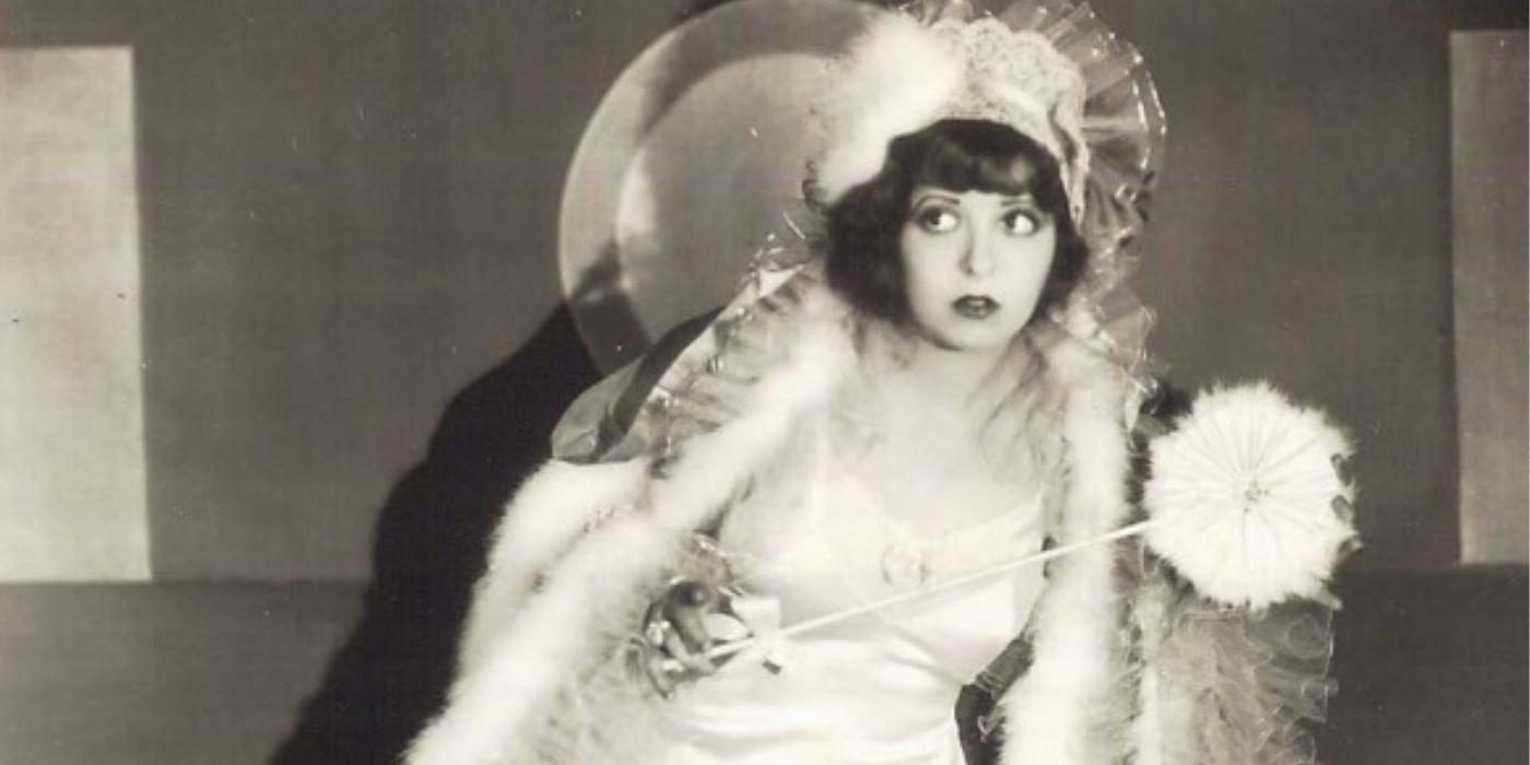 Clara Bow holding a small and white umbrella while wearing a fluffy coat on stage in a scene from 1928&rsquo;s &lsquo;Three Week Ends&rsquo;