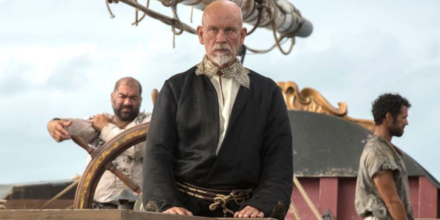Blackbeard, played by John Malkovich, is flanked by two of his pirates as he stands on the forecastle of his ship