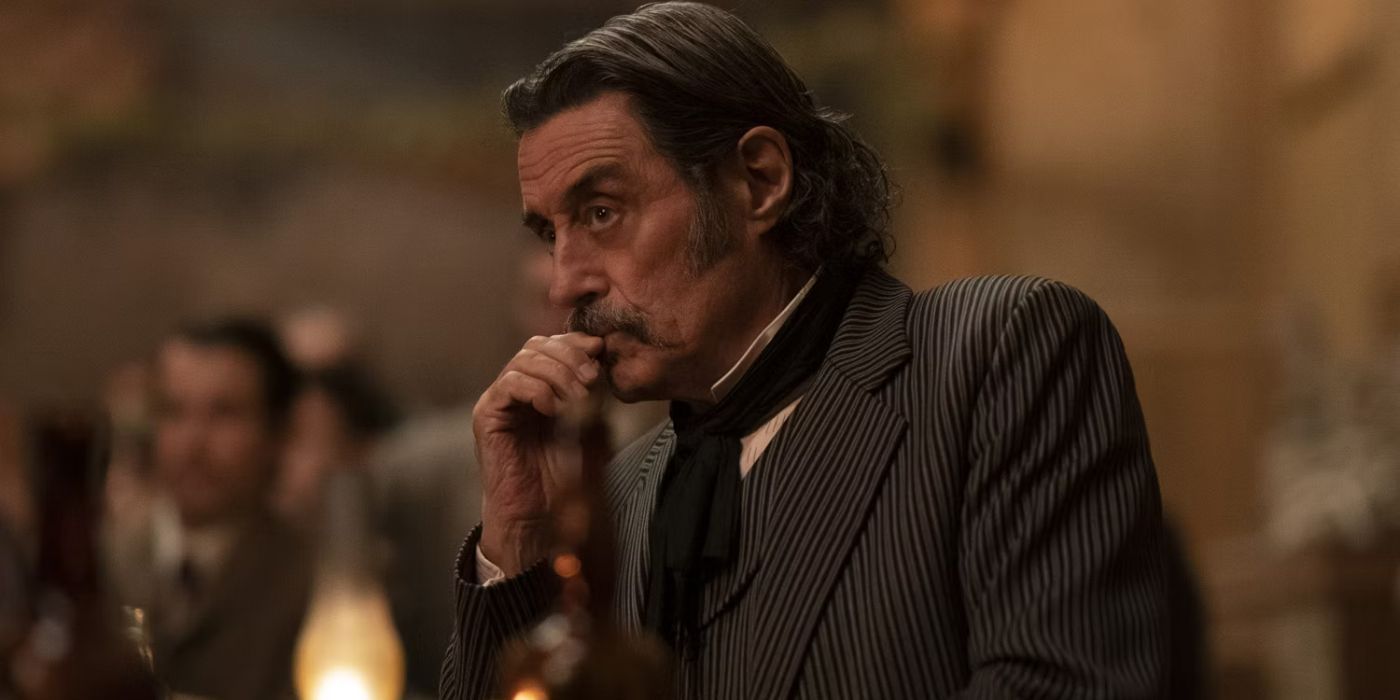 Ian McShane with his hair slicked back and fingers on his mouth looking pensive in Deadwood