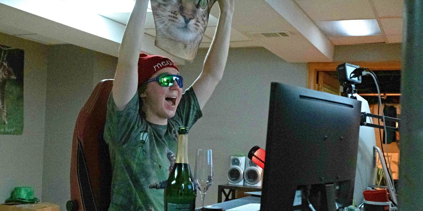 Paul Dano as Keith Gill, holding up an image of a cat face and cheering with champagne in front of him in Dumb Money