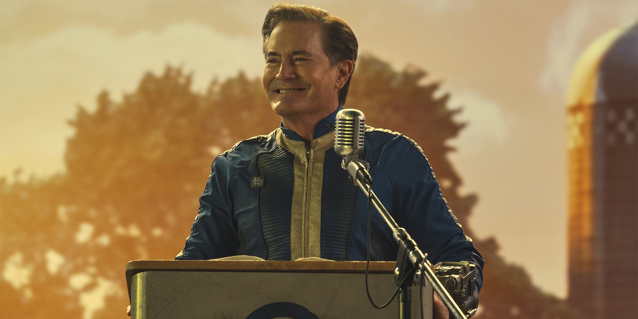 Kyle MacLachlan standing at a podium and smiling in Fallout