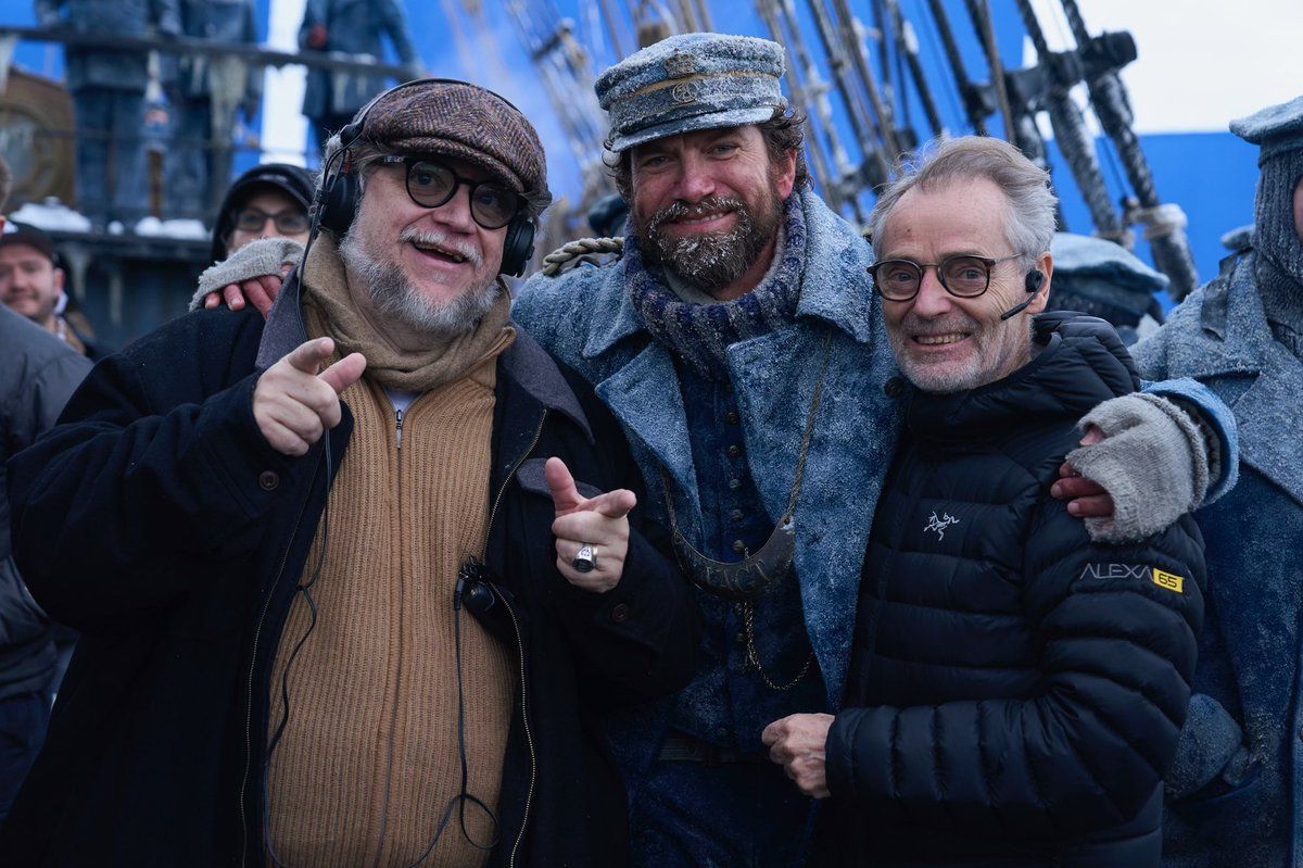 Guillermo Del Toro and two other men on the set of Frankenstein on what looks like a snowy ship