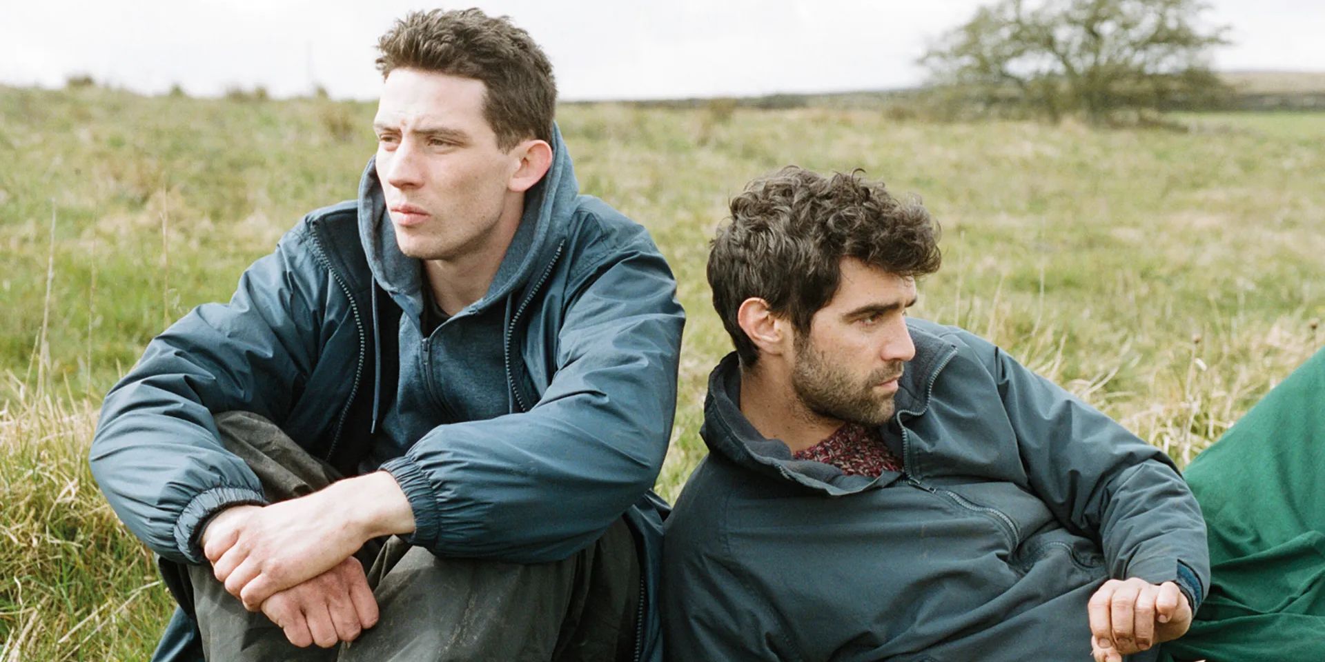 Johnny (Josh O’Connor) and Gheorghe (Alec Secăreanu) sit on a field, staring in different directions.