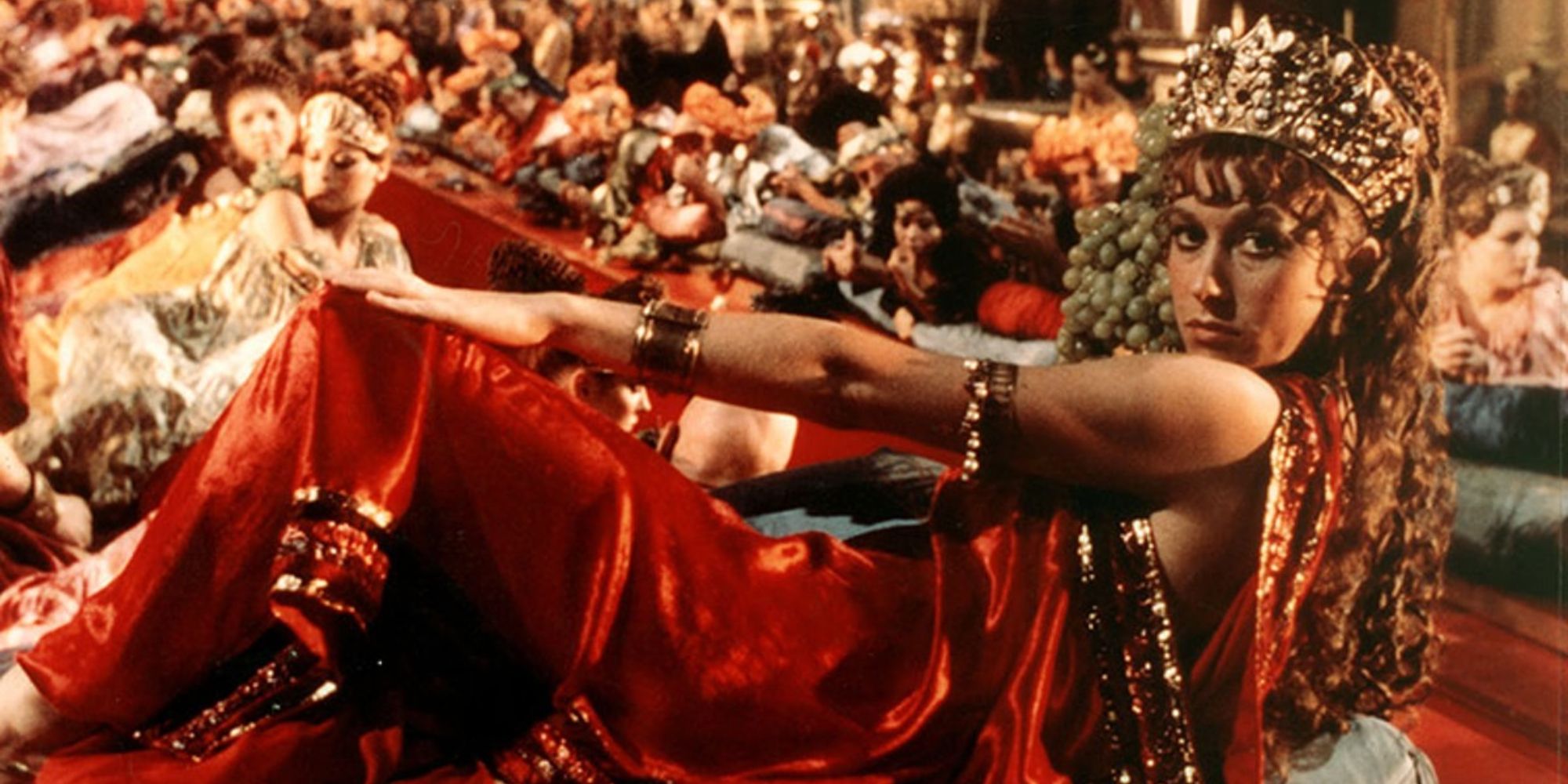 A beautiful woman is lying down dressed in ancient Roman red garb in Caligula (1979)