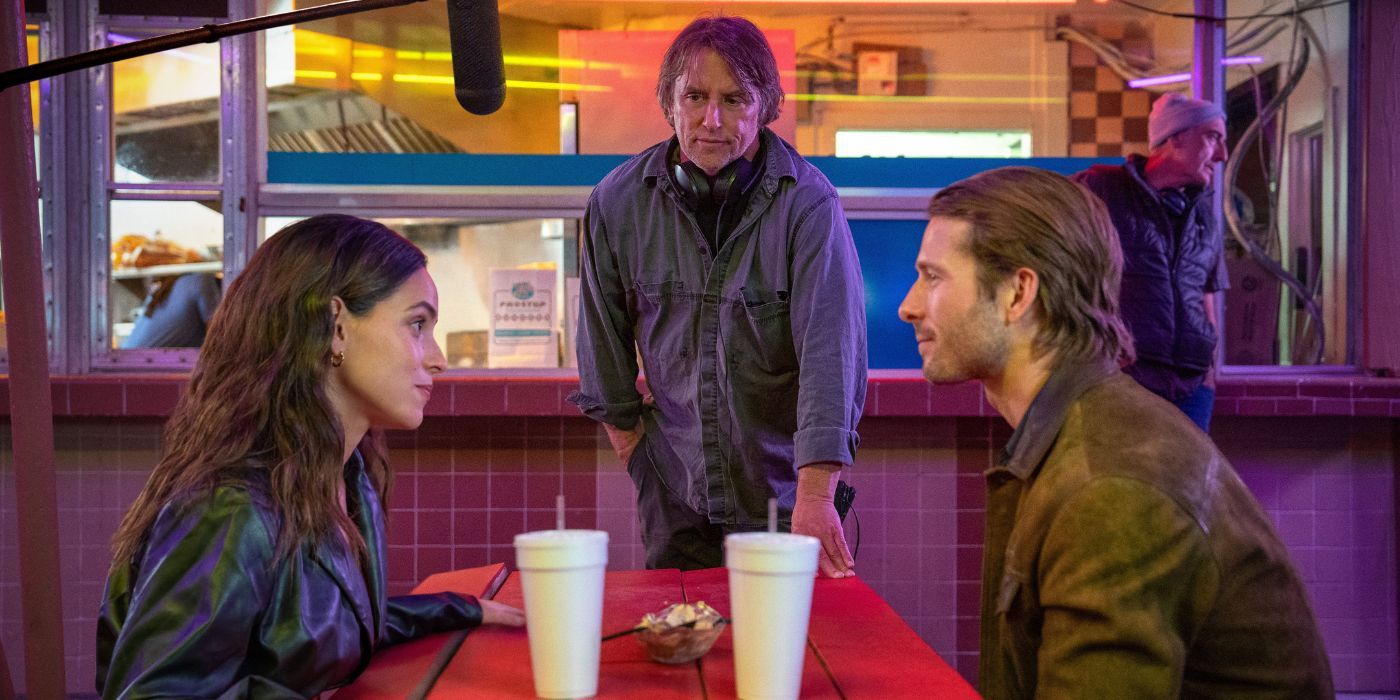 Adria Arjona & Glen Powell sit across from each other at a diner while Richard Linklater directs, in Hit Man