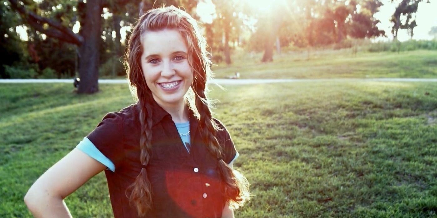 Young Jill Duggar smiling in a field with trees in the background