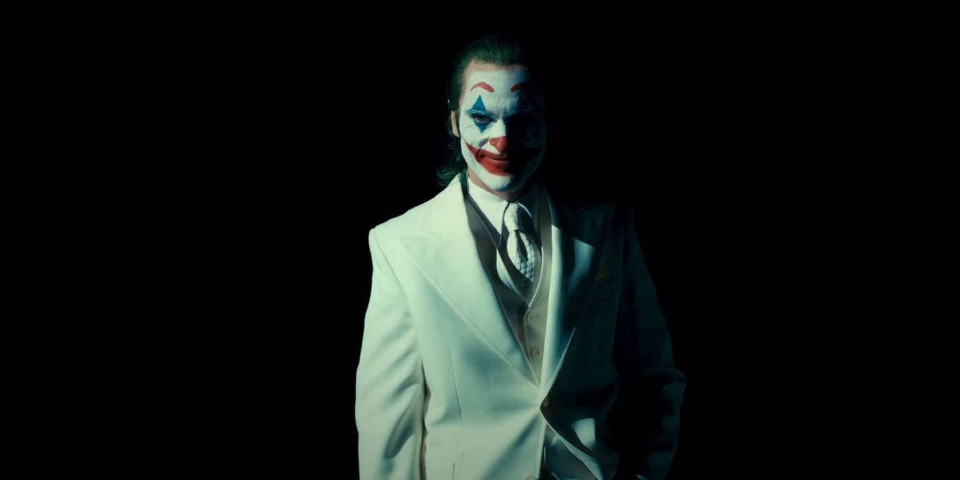 Joaquin Phoenix as Arthur Fleck aka the Joker, wearing a white suit and grinning in Joker: Folie A Deux.