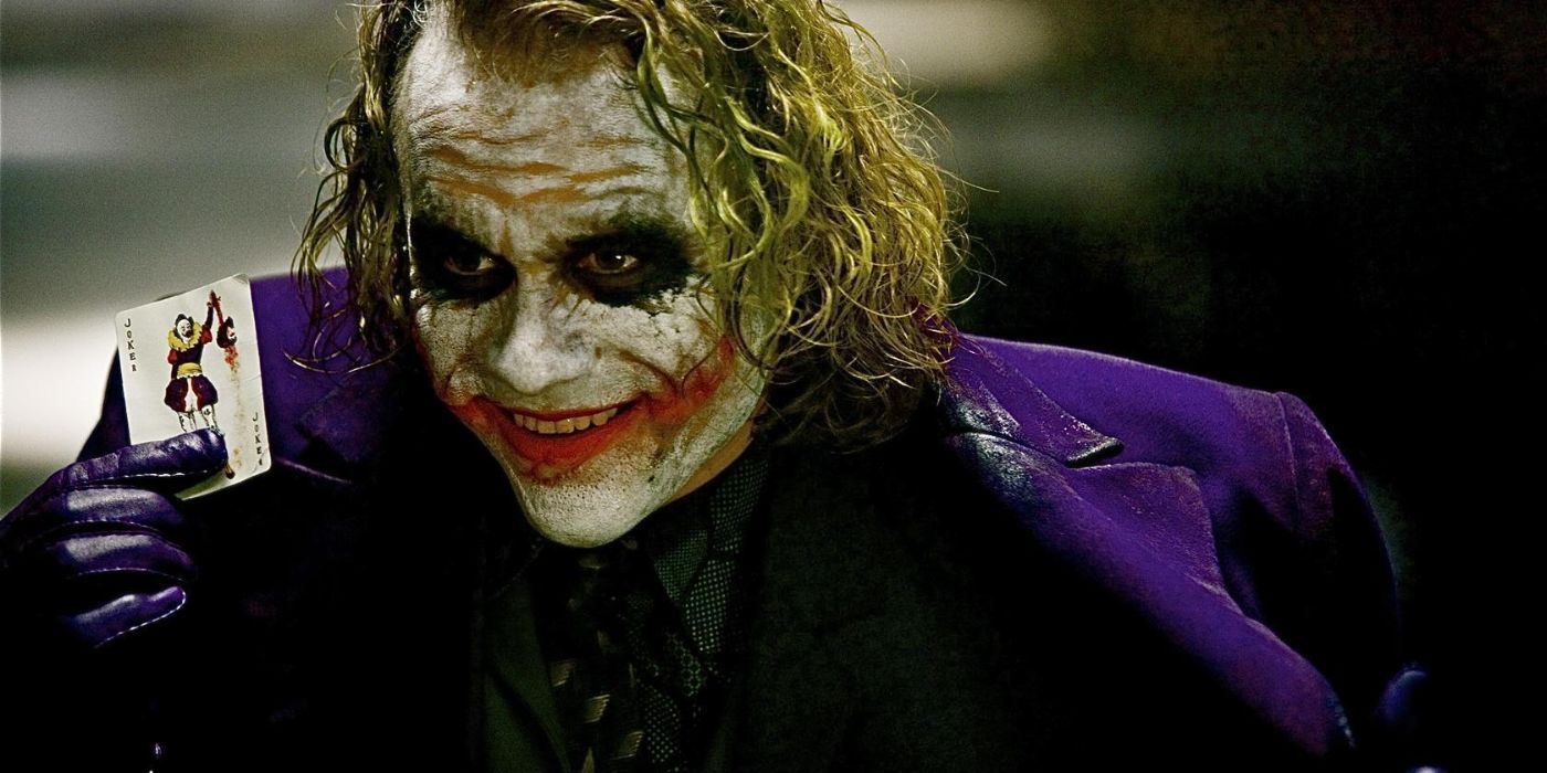 Joker taking a card from his jacket and presenting it while smiling in The Dark Knight