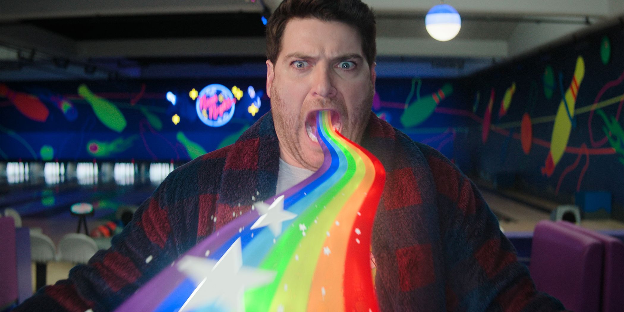 Adam Pally as Wade Whipple dressed in a robe with a rainbow and stars coming out of his mouth on a bowling alley