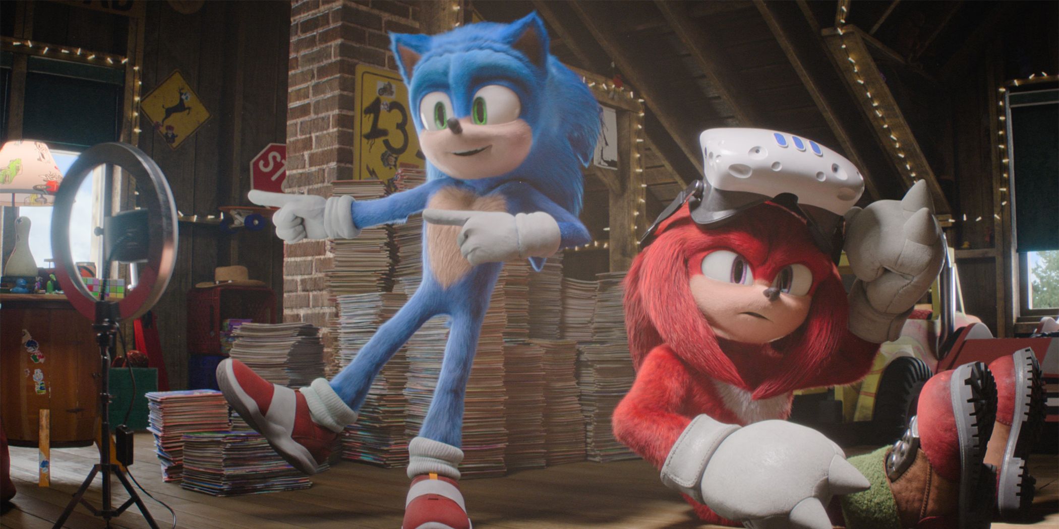 Sonic the Hedgehog salta en el aire frente a la cámara mientras Knuckles juega en realidad virtual junto a él en el ático.