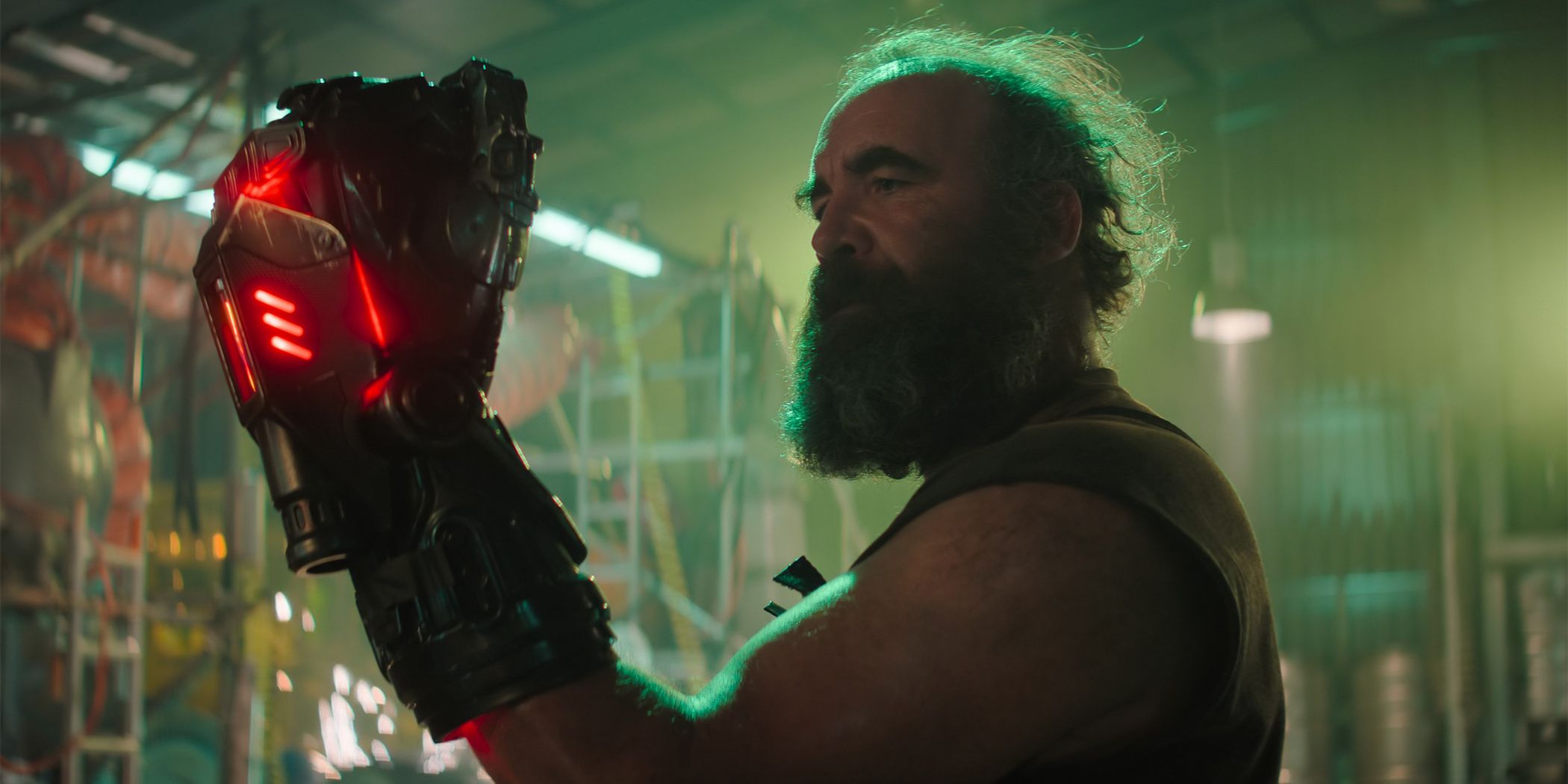 A grizzled Rory McCann as a buyer raises his fist inside a glowing red contraption in a warehouse