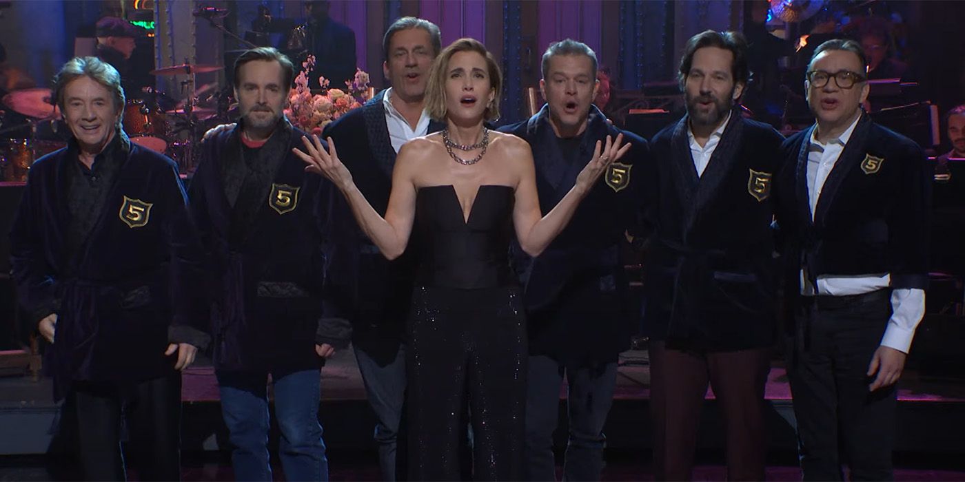 Kristen Wiig standing in front of Martin Short, Will Forte, Jon Hamm, Matt Damon, Paul Rudd, and Fred Armisen on SNL