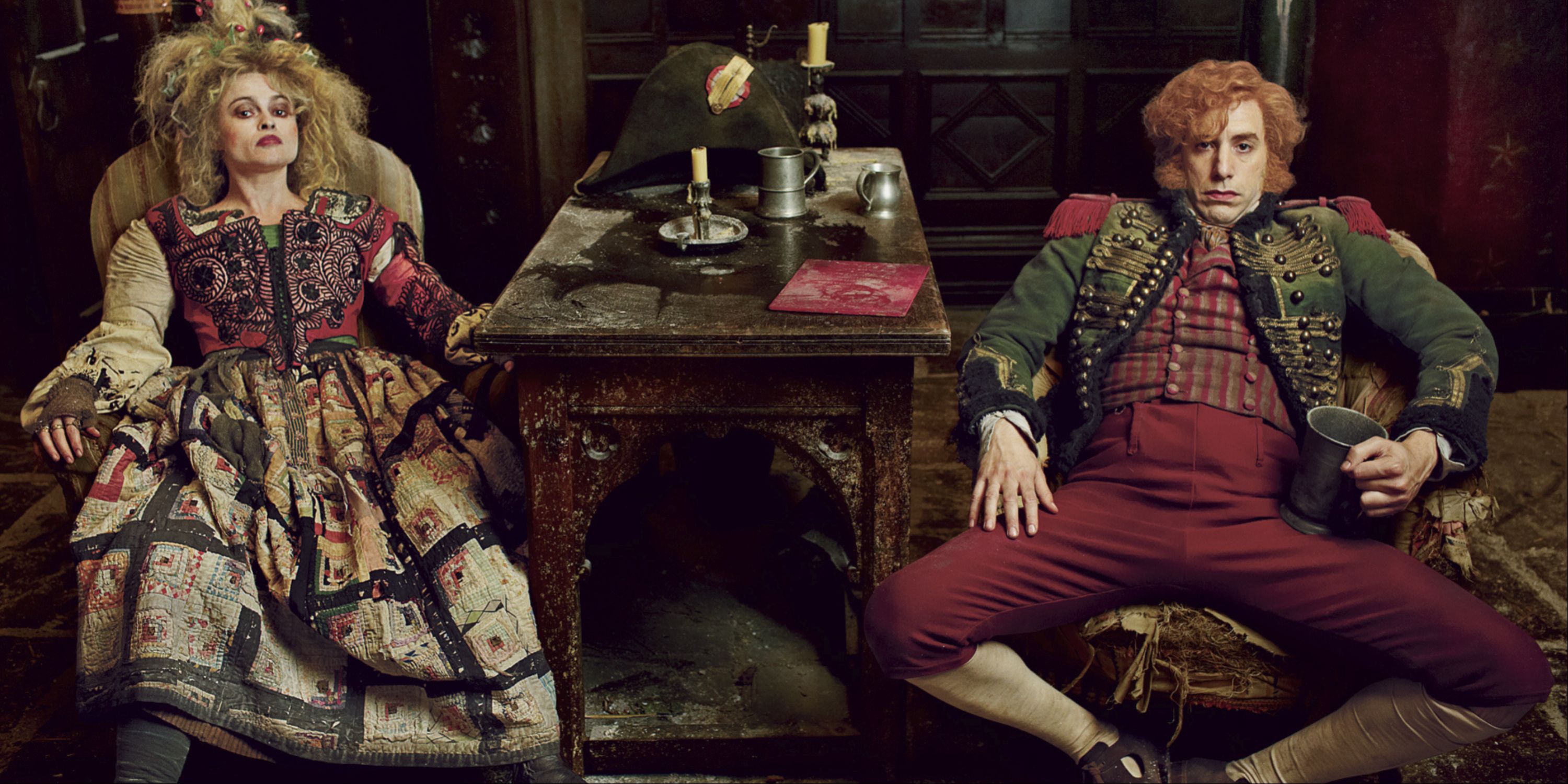 The Thenardiers played by Helena Bonham Carter and Sacha Baron Cohen sit at a table facing the camera in Les Miserables.