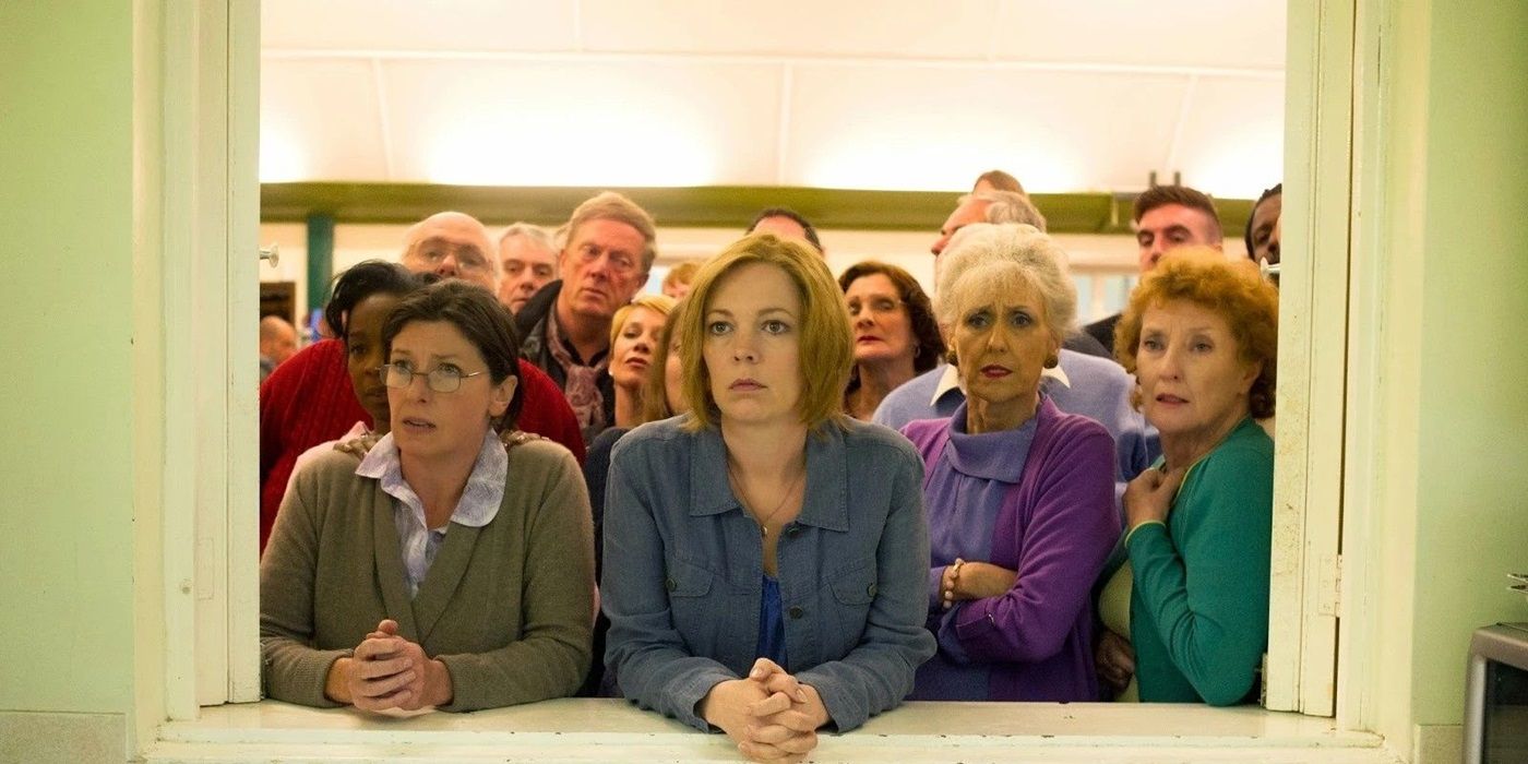 Olivia Colman and the rest of the cast in London Road huddled together and looking through a window