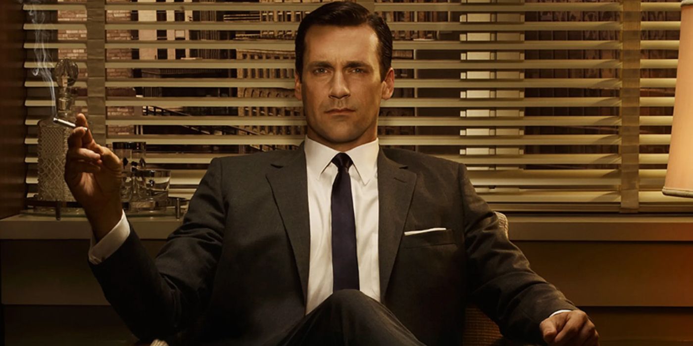Jon Hamm as Don Draper in 'Mad Men' sitting in a chair in his office, legs crossed with a cigarette in his outstretched hand.