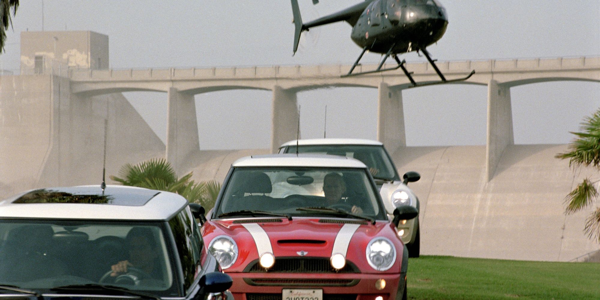 Three mini cooper cars drive across grass as they are chased by a helicopter The Italian Job