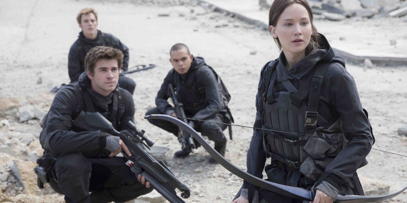 Katniss, played by Jennifer Lawrence, holds her signature bow while a group of armed rebels crouches behind her 