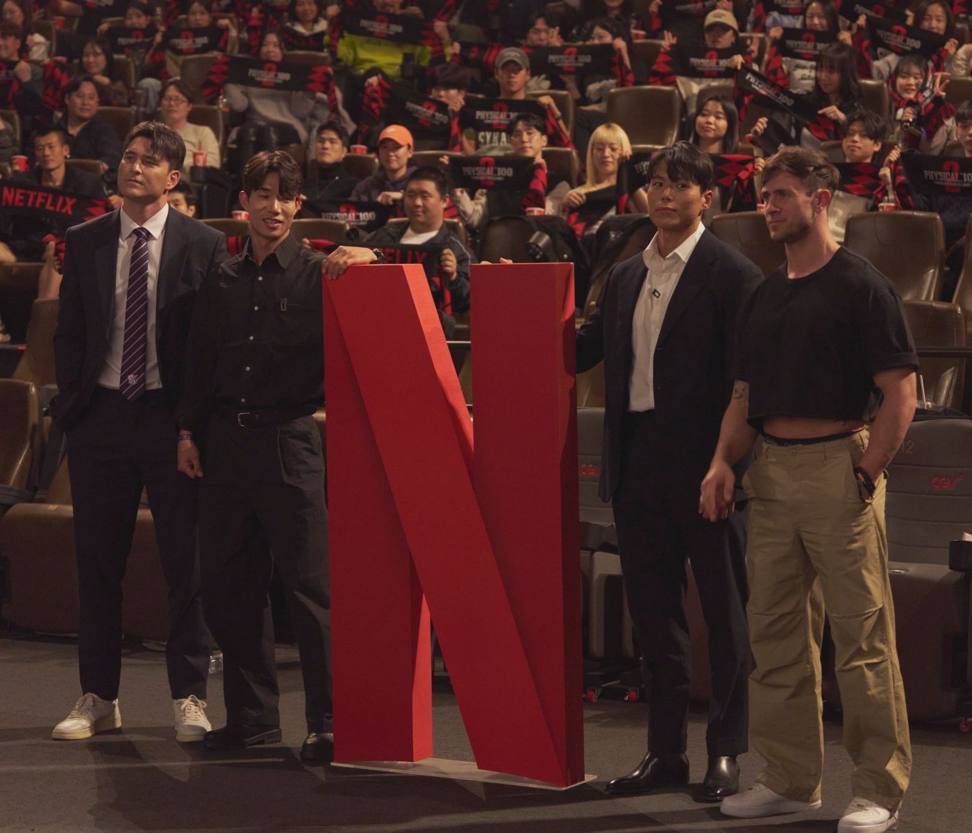 'Physical 100' season 2 final 4 Andre Jin, Beom-Seok Hong, Amotti, and Justin Harvey stand next to the Netflix logo in a movie theater.