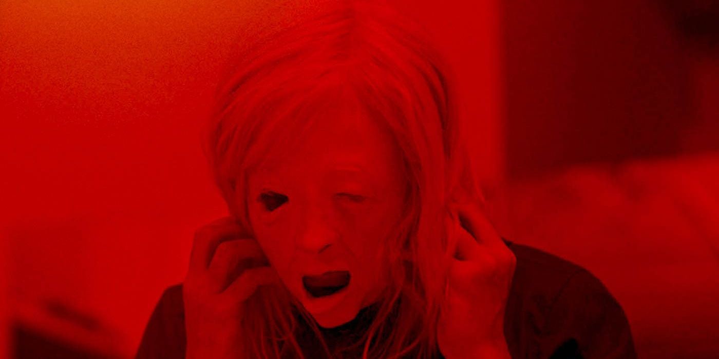 Andrea Riseborough tears an uncanny, distorted mask of a human face from her own face, while cast in stark, red lighting in 'Possessor'