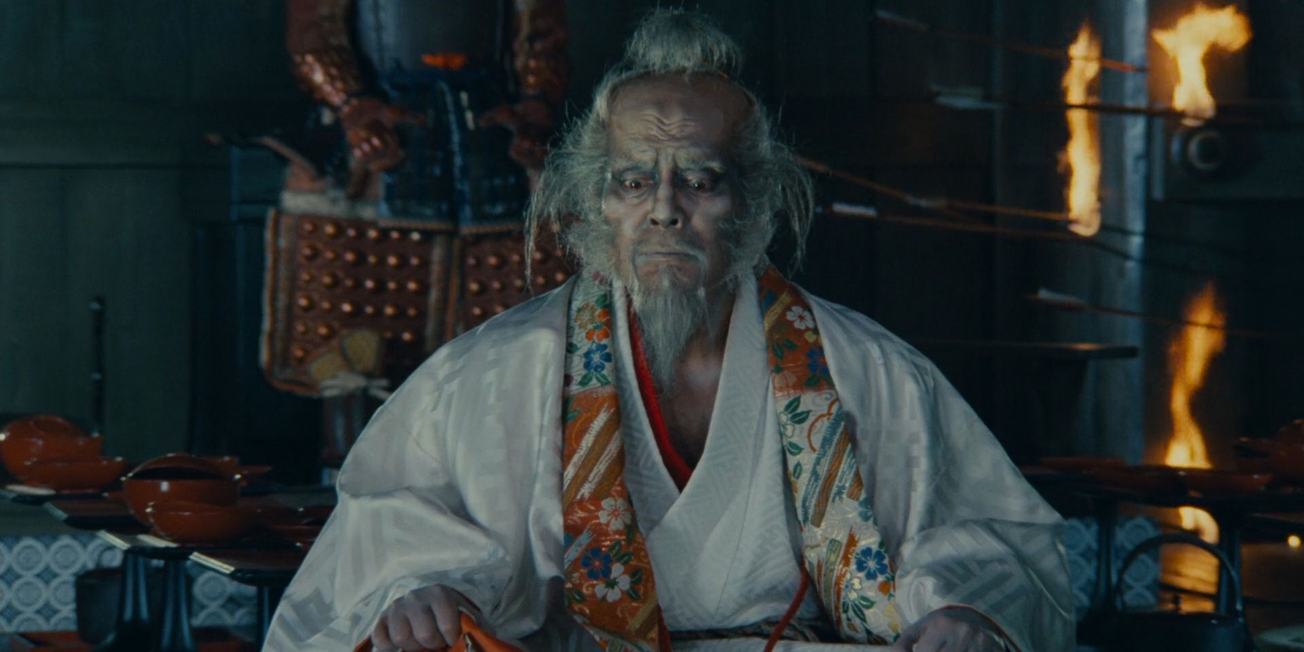 Aging warlord Hidetora?(Tatsuya Nakadai) sits crosslegged to camera, flaming arrows pass behind him.