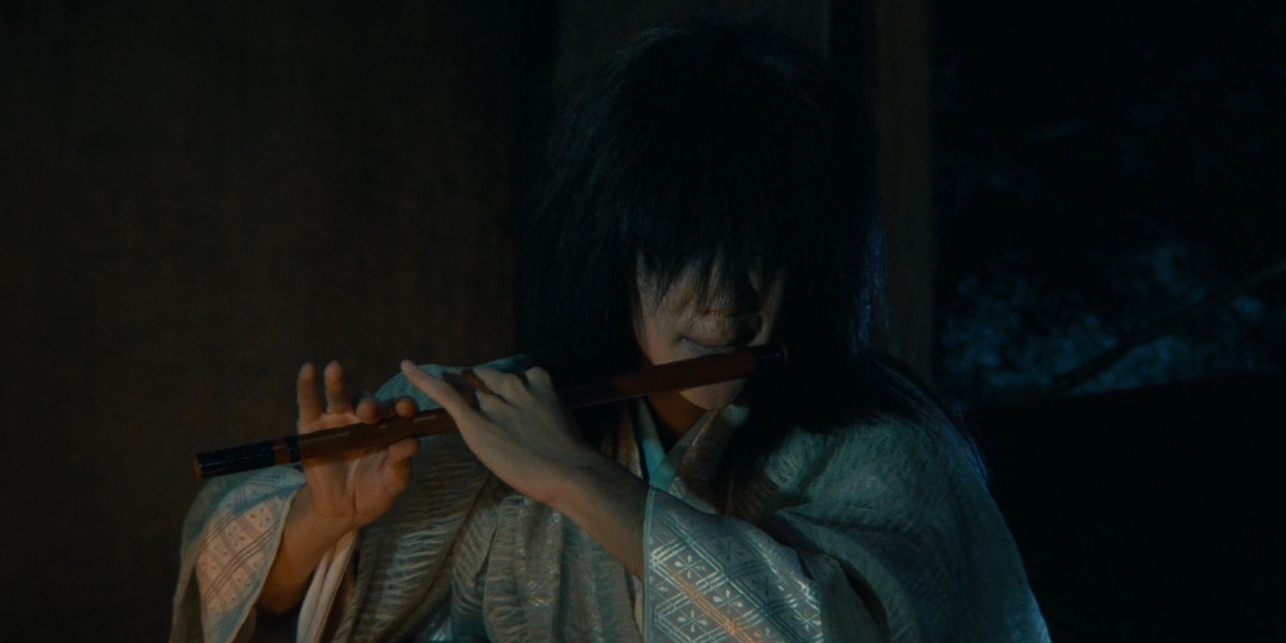 Ran - In darkness, Tsurumaru (Mansai Nomura) plays the flute, lit by firelight. His hair covers his eyes.