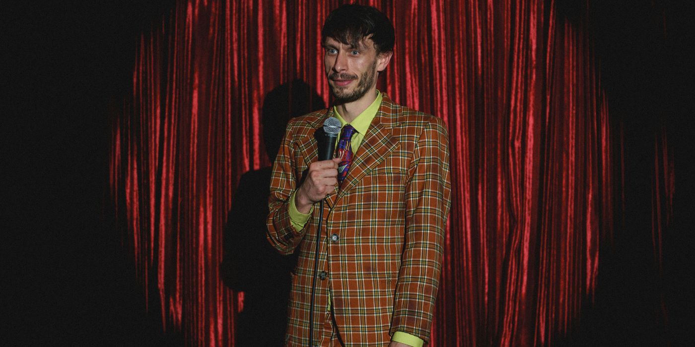 Richard Gadd as Donny wearing a plaid suit while performing on stage in Baby Reindeer.